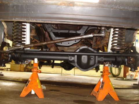 1996 Ford Bronco - The underside of a vehicle is shown, supported by jack stands, highlighting the suspension and drivetrain components.