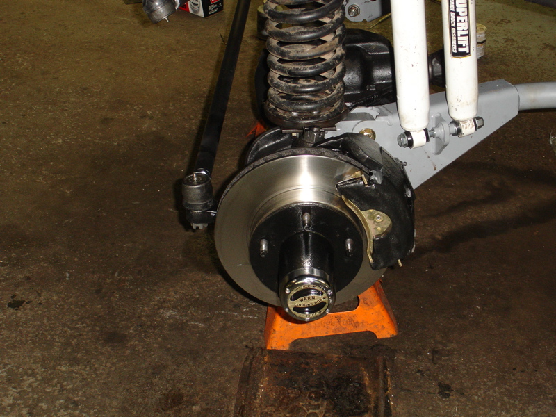 Close-up of a vehicle's front wheel hub, brake rotor, and suspension components, including a coil spring and shock absorber