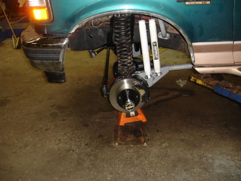 1996 Ford Bronco - The front suspension of a 1996 Ford Bronco is visible, with the wheel removed and the vehicle supported by jack stands.