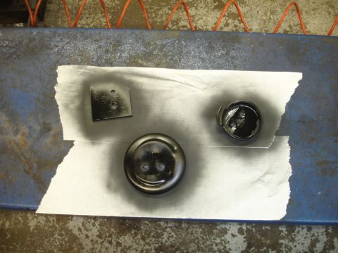 1996 Ford Bronco - Three metal parts, likely automotive components, have been spray painted black and are laid out on a paper towel.
