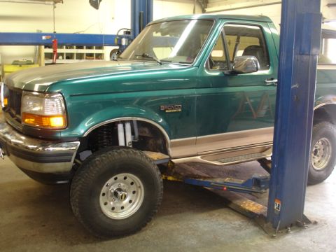 1996 Ford Bronco - A green 1996 Ford Bronco with tan two-tone trim is shown on a vehicle lift in a garage.