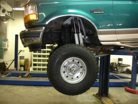 1996 Ford Bronco - A green and tan 1996 Ford Bronco is shown on a lift, highlighting its lifted suspension and front fender detail.