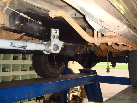 1996 Ford Bronco - Close-up view of the underside of a vehicle, highlighting modified suspension parts and rusty exhaust.