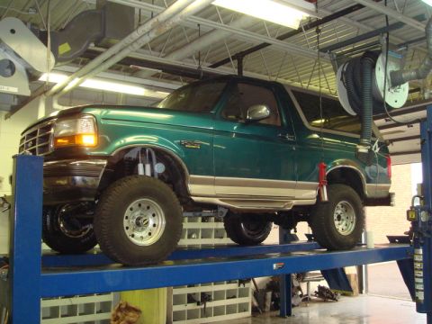 1996 Ford Bronco - A green Ford Bronco is shown on a hydraulic lift inside a service bay.