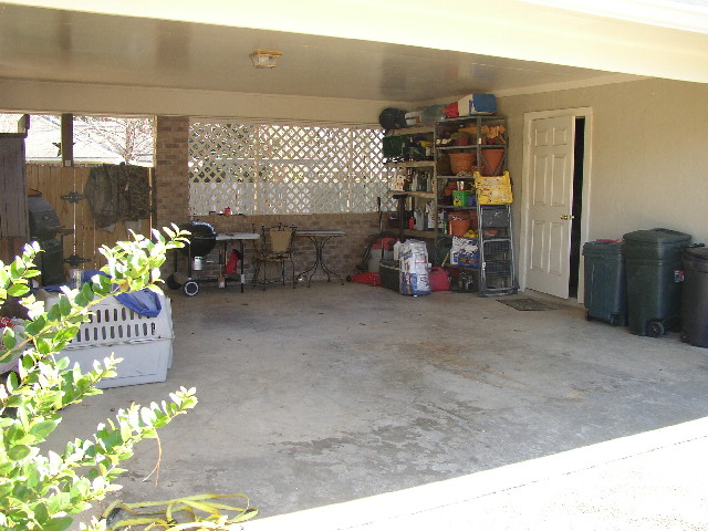 Carport with storage shelves, trash cans, a grill, and plants