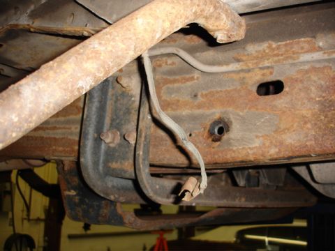1996 Ford Bronco - Close-up view of the heavily rusted undercarriage of a vehicle, showing structural components and brake lines.