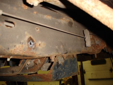 1996 Ford Bronco - Close-up view of a heavily rusted vehicle frame, showing undercarriage components and a cable assembly.