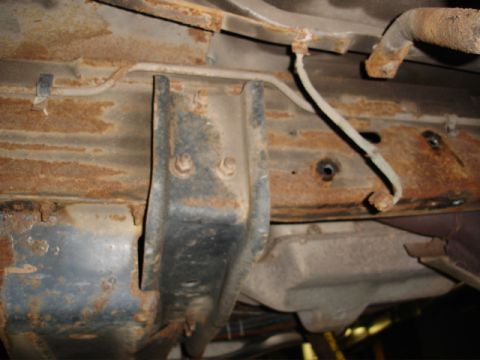 1996 Ford Bronco - The heavily rusted undercarriage of a vehicle shows significant corrosion and damage to its frame and brake lines.