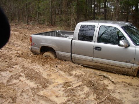 1995 Ford Bronco - A silver pickup truck is deeply stuck in mud, with its tires submerged in the mire.