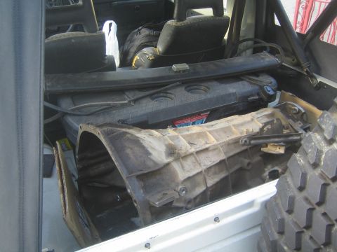 1990 Ford Bronco - dirty plastic transmission tunnel cover and console piece sit removed inside a stripped vehicle interior with off-road tires visible.