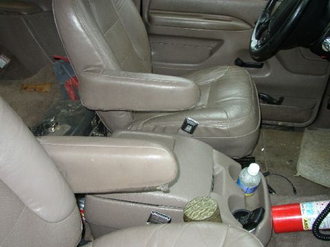 1995 Ford Bronco - The interior of a vehicle is shown, tan leather seats, a center console, a water bottle, and a fire extinguisher.