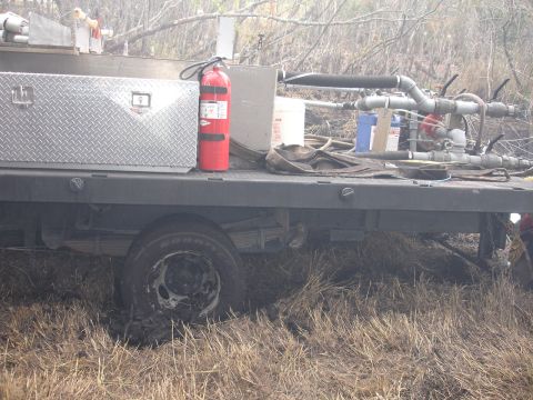 1989 Ford Bronco - Flatbed truck equipped with a fire extinguisher and pumping equipment is stuck in muddy terrain.