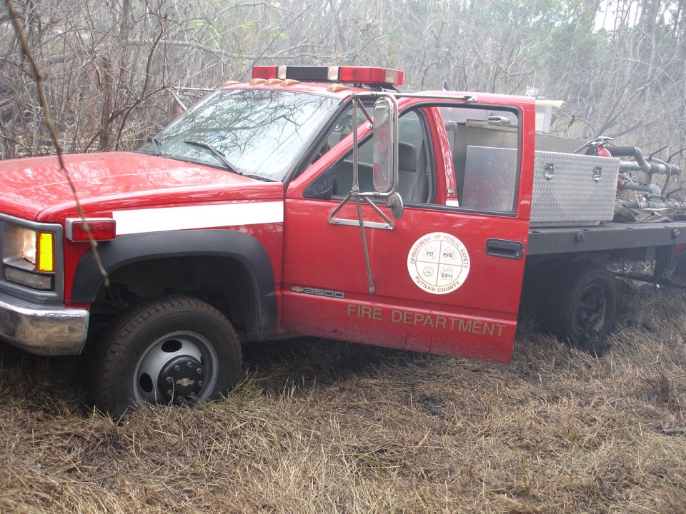 red fire department truck with white stripe, parked in dry grass