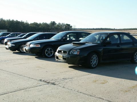 2001 Mercury Grand Marquis - Several black sedans are parked in a line on a paved surface under a clear sky.