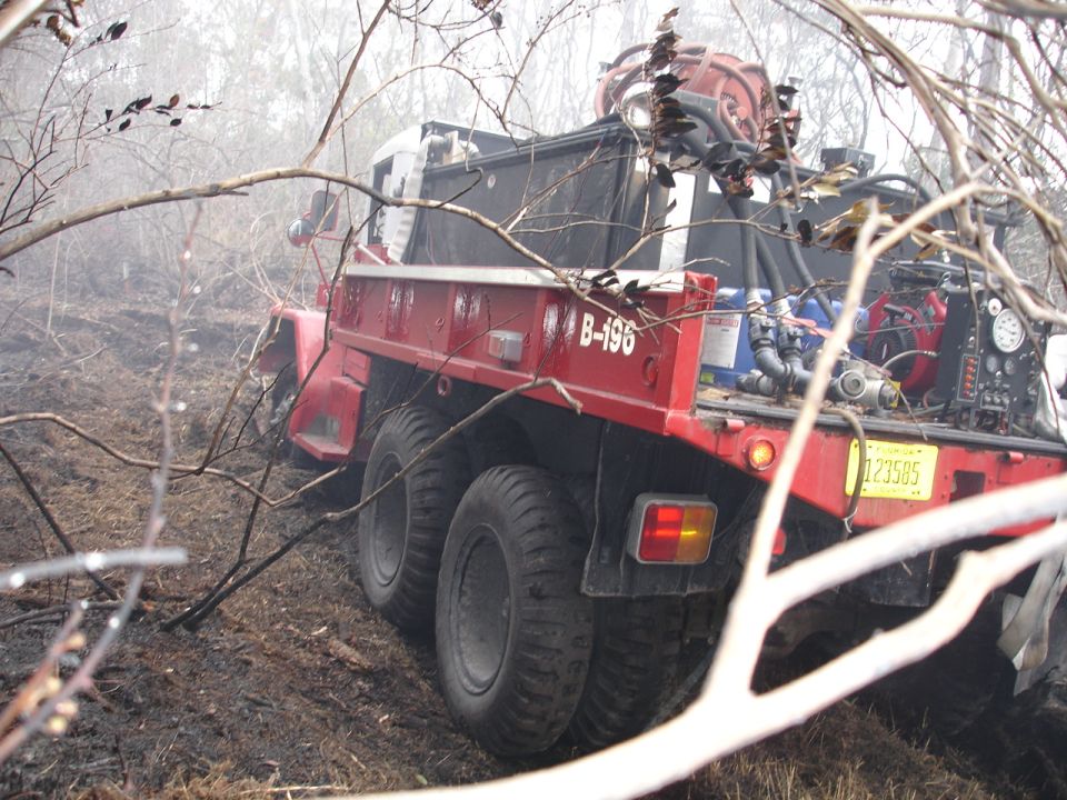 Red fire truck with multiple rear wheels in a wooded area