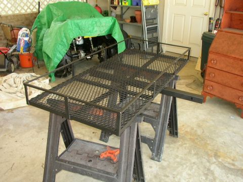 1995 Ford Bronco - A vehicle is partially visible under a green tarp, with a cargo rack supported by sawhorses in front of it.