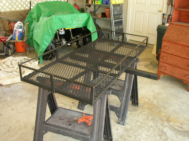 Black steel hitch-mount cargo carrier with mesh deck and side rails resting on sawhorses in a garage