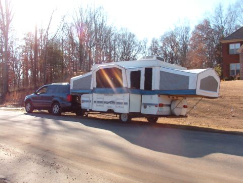 1975 Ford Bronco - A dark blue SUV is seen towing a white pop-up camper down a residential street.