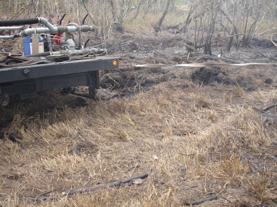 Rear view of truck bed with water pump and hose, in a dry, wooded area