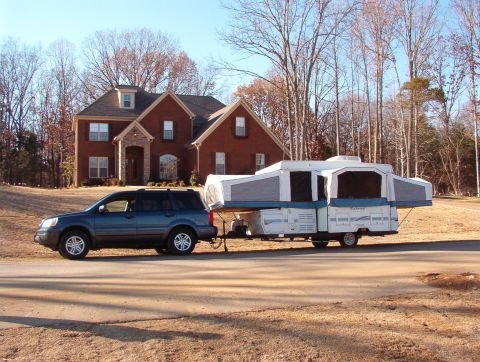 1975 Ford Bronco - SUV towing a pop-up camper down a residential street.
