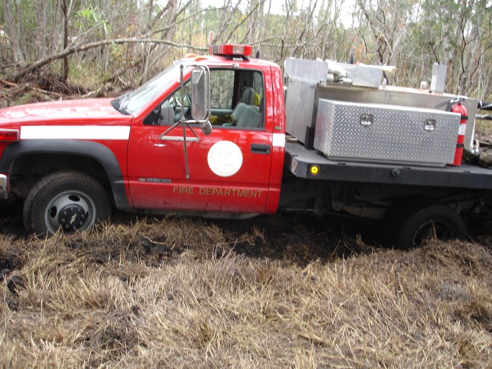 Red fire truck with "FIRE DEPARTMENT" on the door is stuck in muddy terrain with dry grass