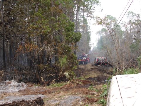 1989 Ford Bronco - Fire trucks navigate a muddy path in a wooded area, possibly after a fire.