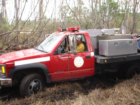 1989 Ford Bronco - A red fire department truck is seen driving through a wooded, muddy area.