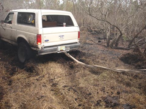 1989 Ford Bronco - White 1989 Ford Bronco is stuck in thick mud and appears to be pulling out fire trucks.