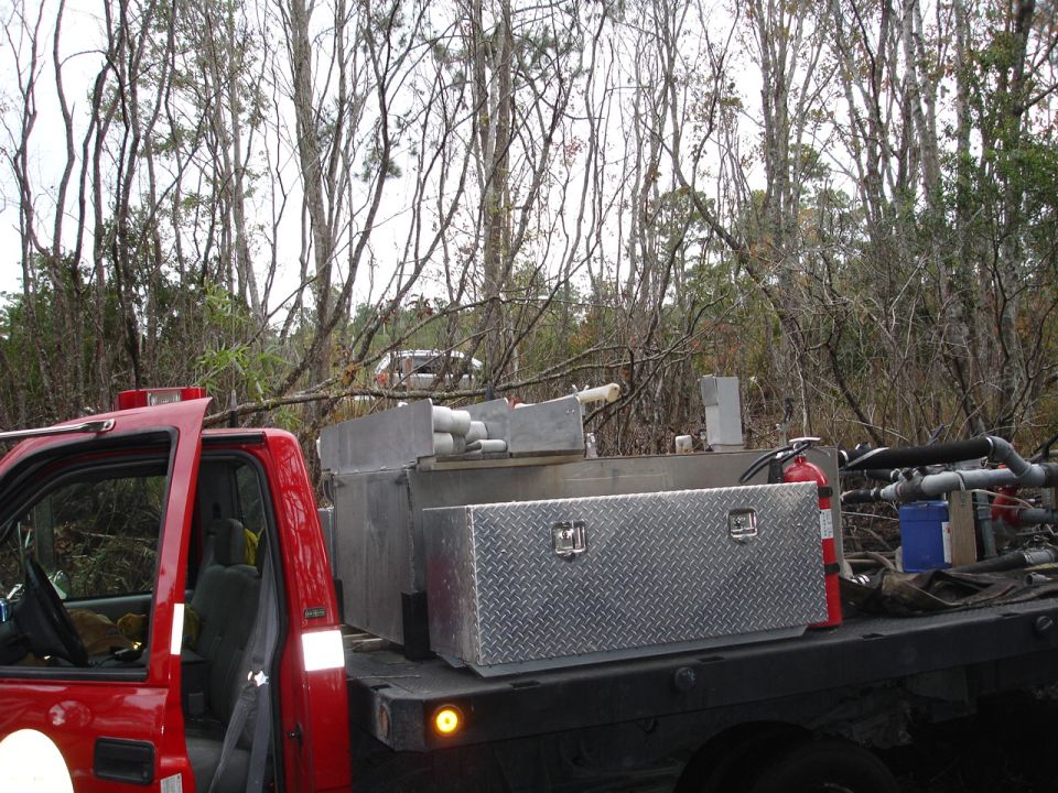 red flatbed truck with a large water tank and diamond plate toolbox mounted in the bed, fire extinguisher visible