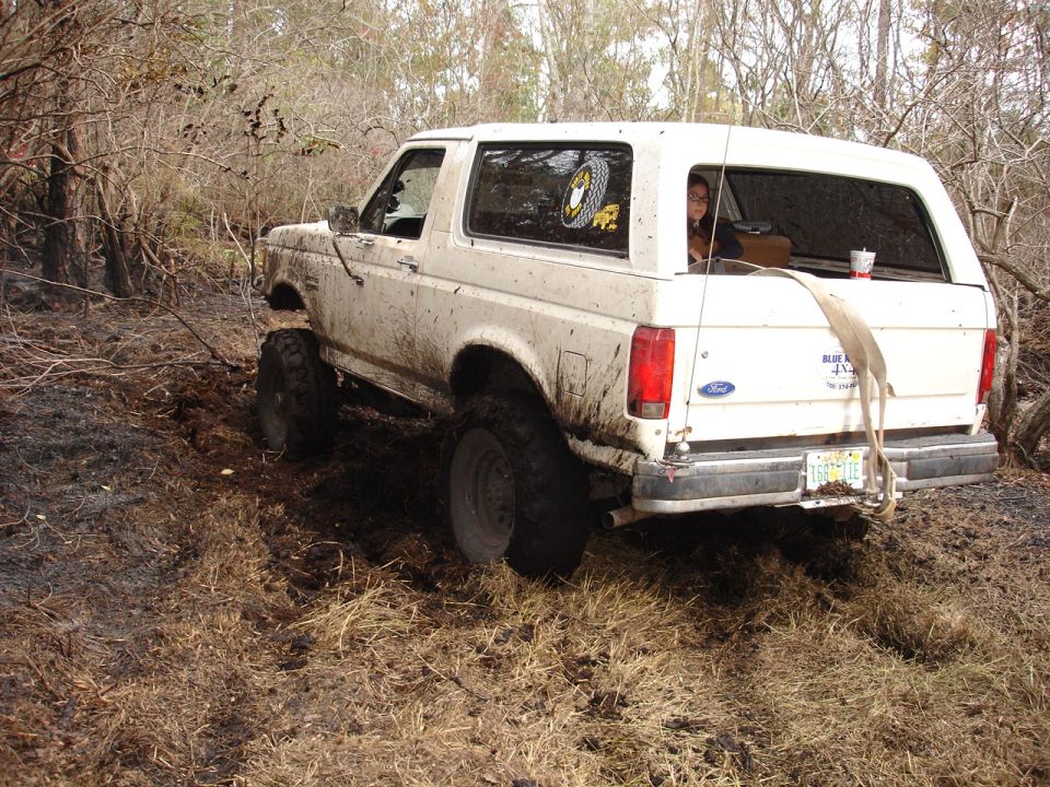 Mud-covered white Ford Bronco with lifted suspension driving off-road
