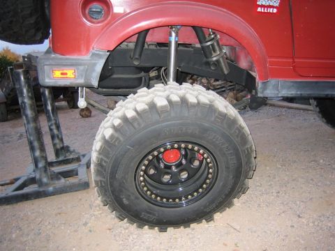 1987 Suzuki Samurai - Close-up view of the suspension and large off-road tire on a red vehicle.