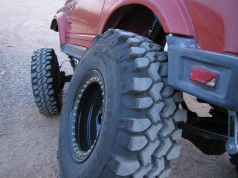 1987 Suzuki Samurai - A modified 1987 Suzuki Samurai sits on a gravel surface, its massive off-road tires and lifted suspension.