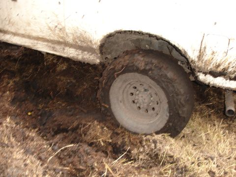 1989 Ford Bronco - A white vehicle's tire is deeply embedded in mud and vegetation, indicating it is stuck.