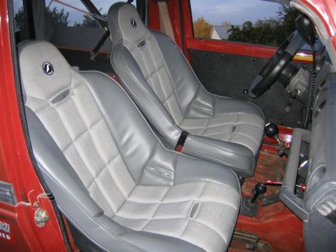 1987 Suzuki Samurai - The interior of a red vehicle features grey bucket seats, a roll cage, and a manual transmission shifter.