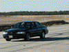2001 Mercury Grand Marquis - A black sedan is captured in motion on a dusty, unpaved road under a clear sky.