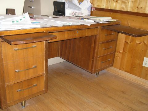1990 Ford Bronco - A cluttered wooden desk with multiple drawers and papers on top, set against a wood-paneled wall.