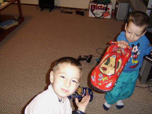 Young boy in white shirt holds a blue toy car, another boy in Mickey Mouse shirt holds a red toy car