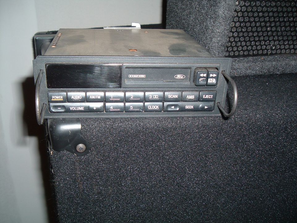 Ford car stereo with buttons for Power, Audio, AM/FM, Volume, 3 CD, Scan, AMS, Eject, Clock, and Seek