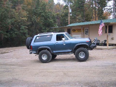 1995 Ford Bronco - This lifted SUV, likely from the 1980s, is parked in front of a building with an American flag.