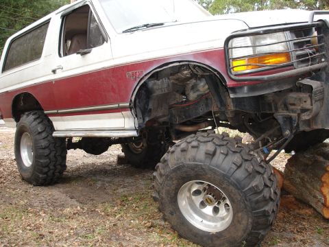 1989 Ford Bronco - Modified Ford Bronco with oversized tires and suspension modifications sits on uneven terrain.