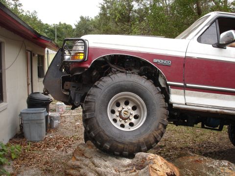 1989 Ford Bronco - This modified Ford Bronco is positioned on a large log, showing its off-road capabilities.