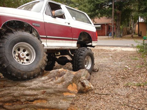 1989 Ford Bronco - This modified Ford Bronco is shown with oversized tires, navigating over a large log.