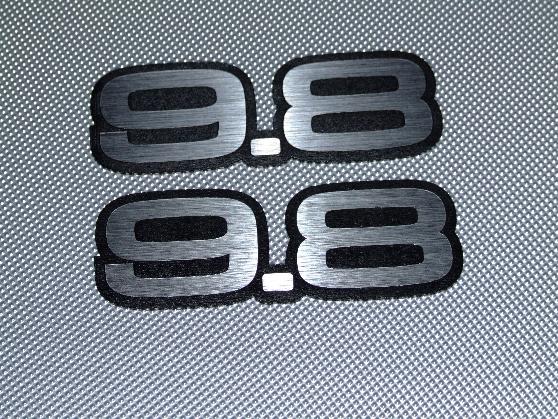 Two black and silver "9.8" emblems on a textured gray surface
