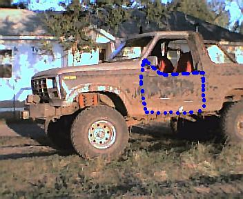 1984 Ford Bronco - A lifted Ford SUV with the top removed, caked in dried mud, parked on grass with oversized mud tires on white wagon-style wheels and a tube…