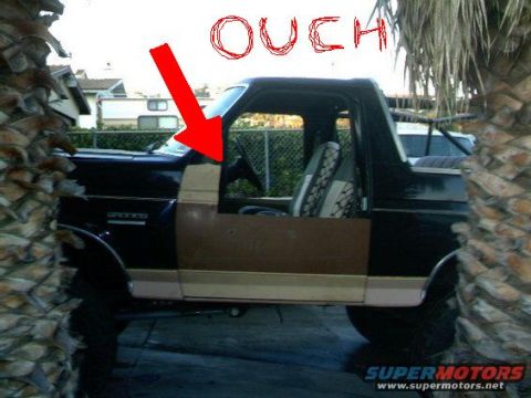 1984 Ford Bronco - Side view of a black and tan two-tone Ford Bronco with the top and doors removed, parked on a driveway between palm trunks, with a hand-dra…