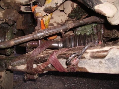 2000 Chevrolet Tahoe - Close-up view of a vehicle's greasy steering and suspension components, with a red strap securing a part.