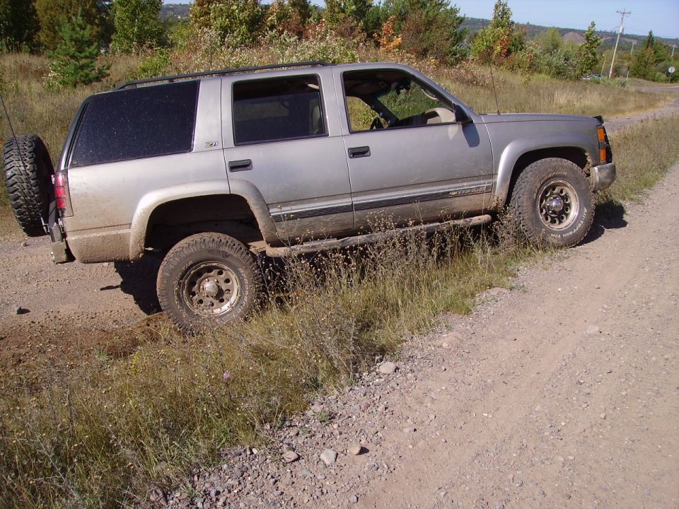 Silver 2000 Chevrolet Tahoe parked on a dirt road with grass on the side, spare tire mounted on the back