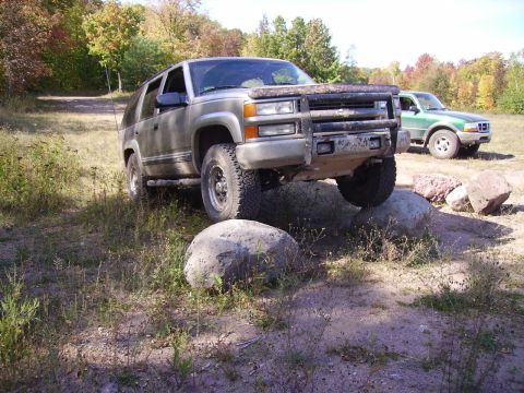 2000 Chevrolet Tahoe - Silver SUV navigating rocky terrain with a green truck visible in the background.