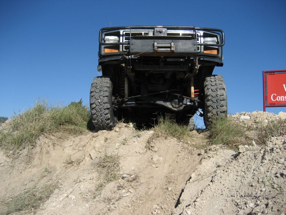 Front view of a lifted truck with large tires climbing a dirt hill