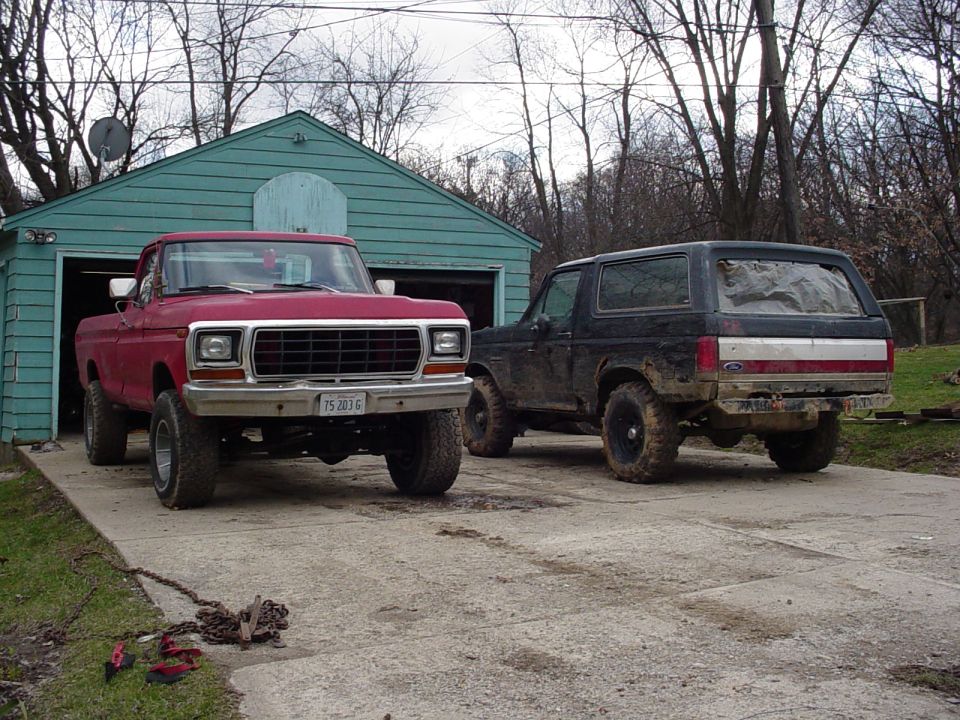 Black 1988 Ford Bronco parked next to a red Ford pickup truck